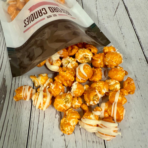 Orange popcorn with white drizzle spilling out of a bag on a wooden surface.