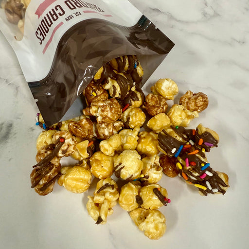 Assorted popcorn with chocolate drizzle and sprinkles spilling out of a bag on a marble surface.